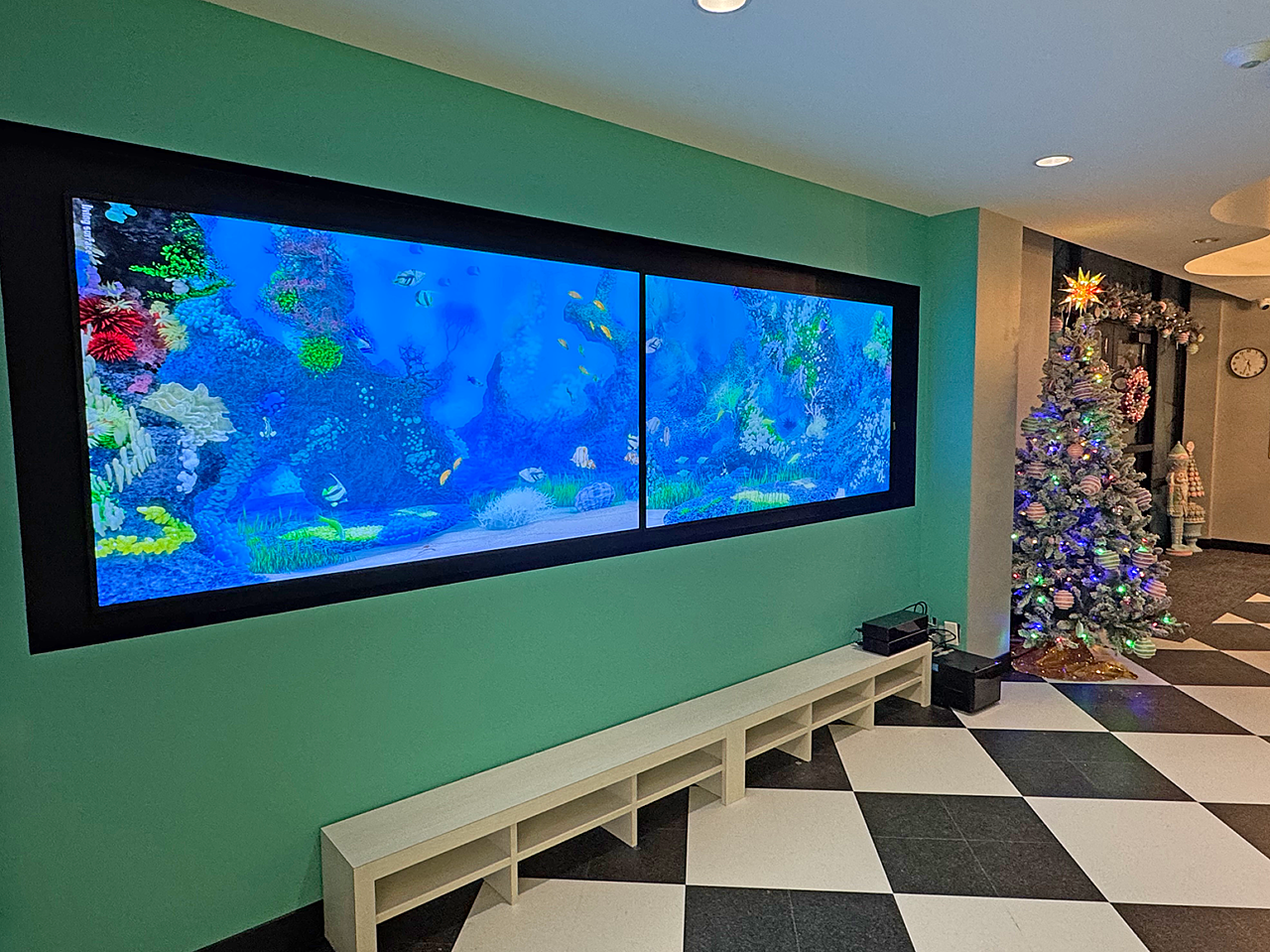 Riley ABA:  Teel wall in dining room has a full-size tv with a digital fish tank. A small bench with cubbies line the wall. Black/white checked tile floor
