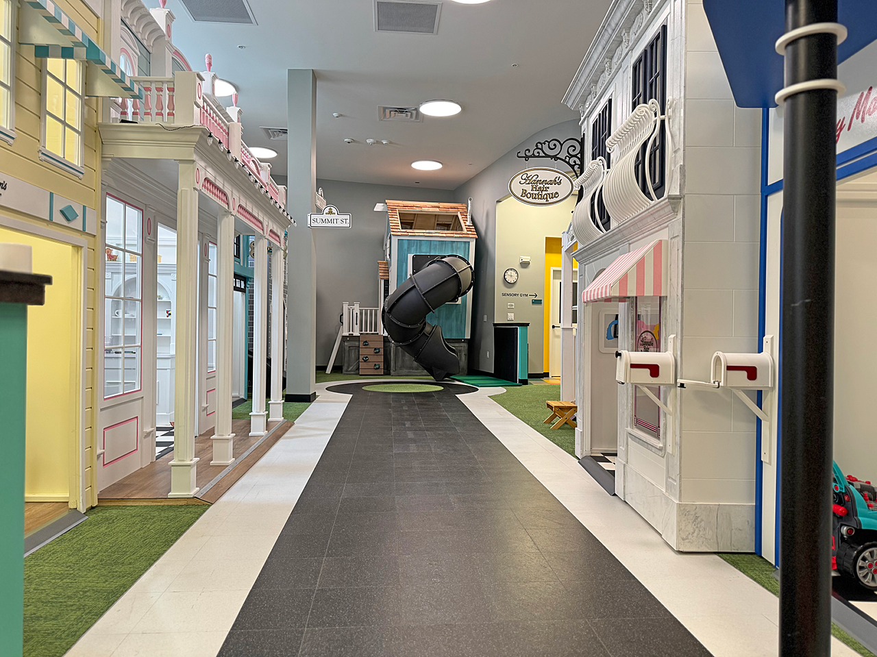 Riley ABA: Kid-sized town with replicas of storefronts in pastels on both sides. Floor of black floor tiles replicate street. A small "park" is at the end.
