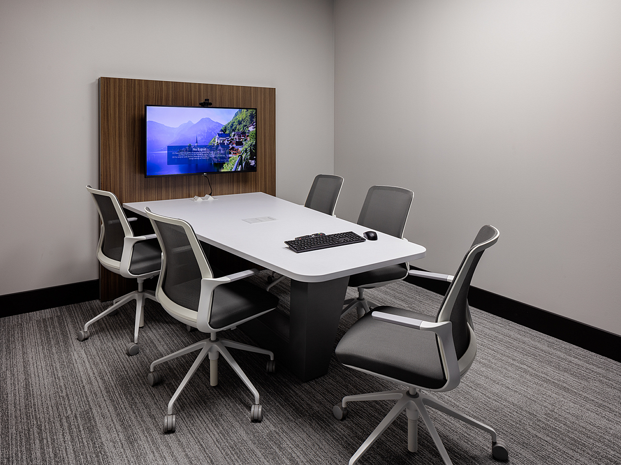 Dr Vince huddle room with angled table, rolling chairs and a attached wood veneer wall panel with tv screen.