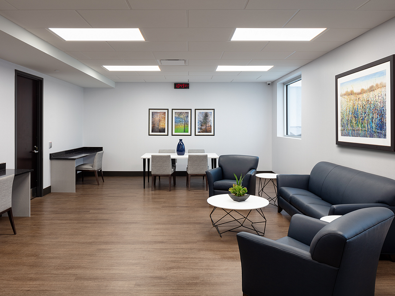 Dr Vince Clinical Research-patient lounge with blue leather couch/armchairs, coffee & side tables w/ plant and 4-person table. Counter workstations/chair
