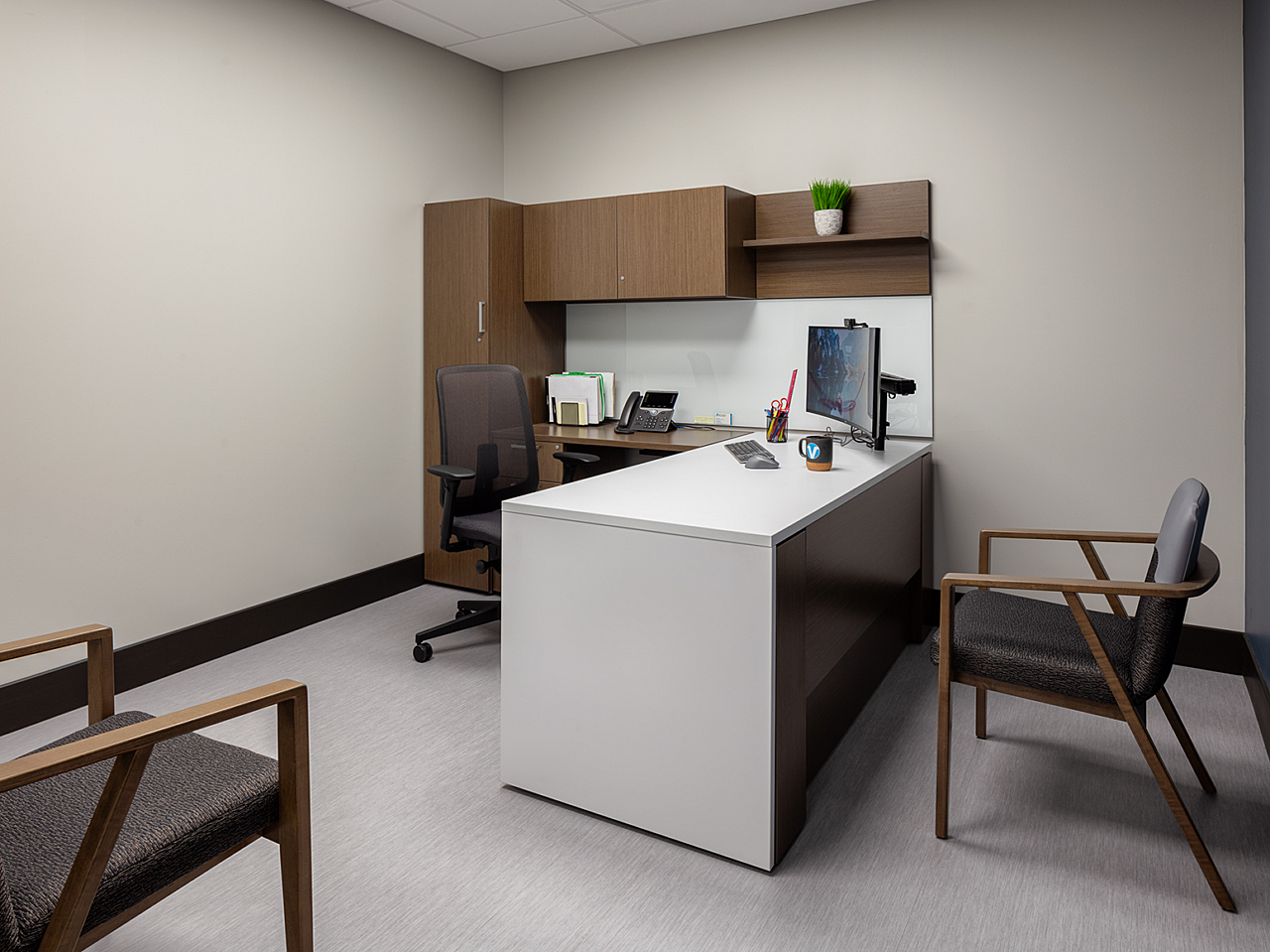 Dr Vice Private Office with white waterfall edge desk, dark woodgrain cabinets with shelf, black task chair and two blue/wood side chairs.