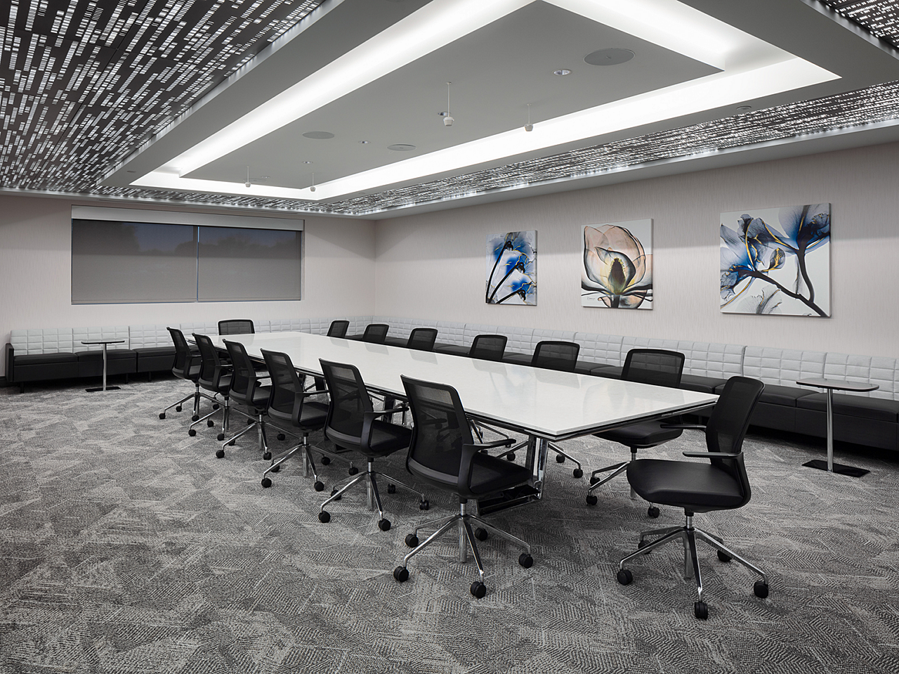 Dr Vince large conference room with large table and rolling chairs. Grey banquette seating along two walls. Floral paintings & architectural ceiling/lights
