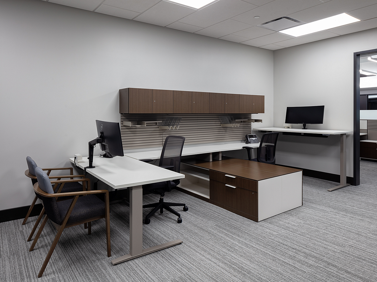 Two large height-adjustable workstations with shared wall,counter and storage space. Blue/dark wood side tables and black task chairs.