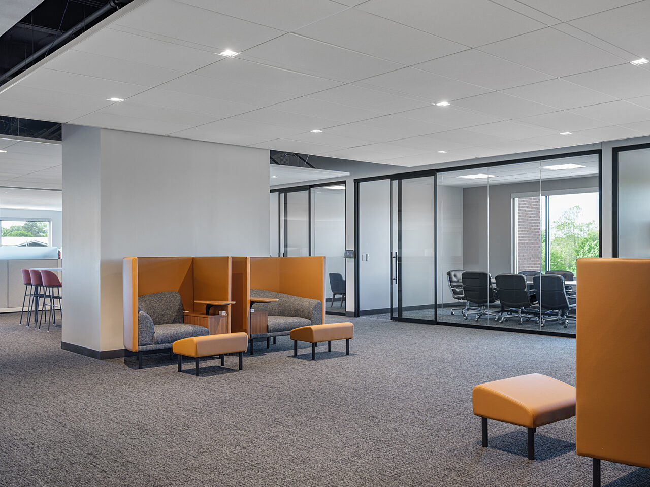 Open area with a collaborative space behind a small wall and e yellow/grey high backed booths with matching ottomans and attached desktops for focus work