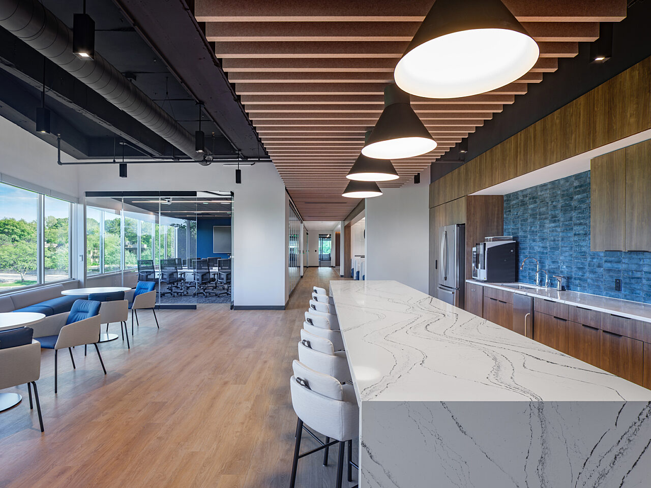 Breakroom marbled waterfall table with white stools, wooden ceiling accents, blue bankquette seating with white cafe chairs and blue tiled backsplash