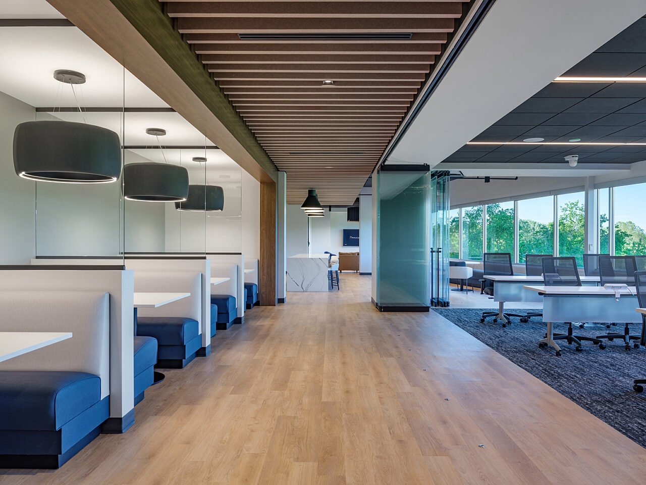 A long corridor is lined by a training room with accordion walls opened and blue/white cafe booths with hanging grey drop lights that resemble tires