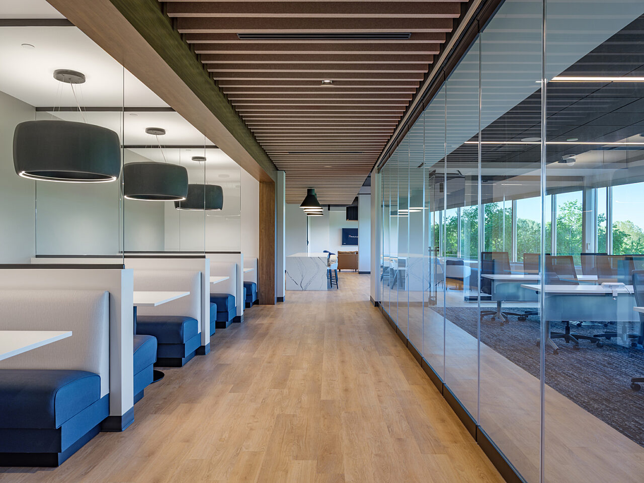 A long corridor is lined by the walls of a company training room on the right and blue/white cafe booths with hanging grey drop lights that resemble tires