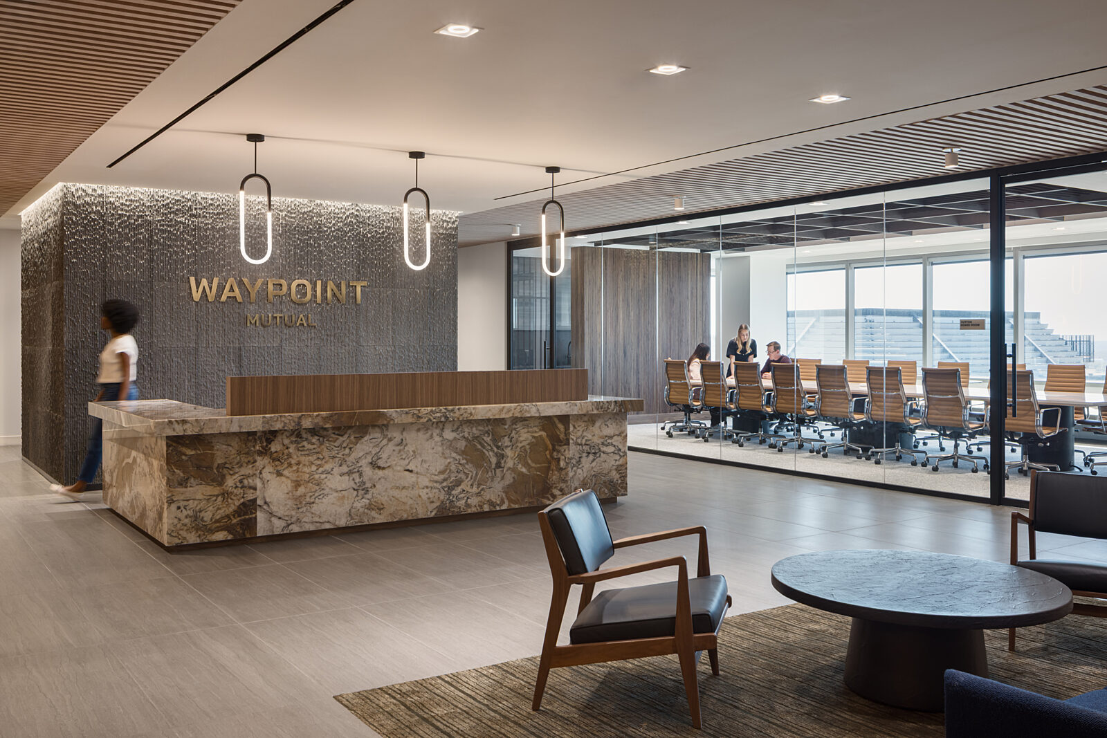 Waypoint Mutual reception area with glass-walled view of boardroom. Marbled reception desk, lounge seating area on area rug, deep browns, cream and whites.