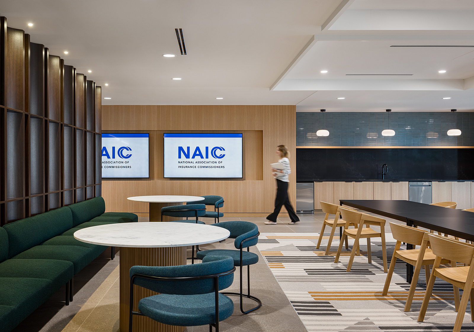 NAIC breakroom with modern banquette seating in rich green and blues, long darkwood tables with caramel colored wood chairs, NAIC logo on tv screens