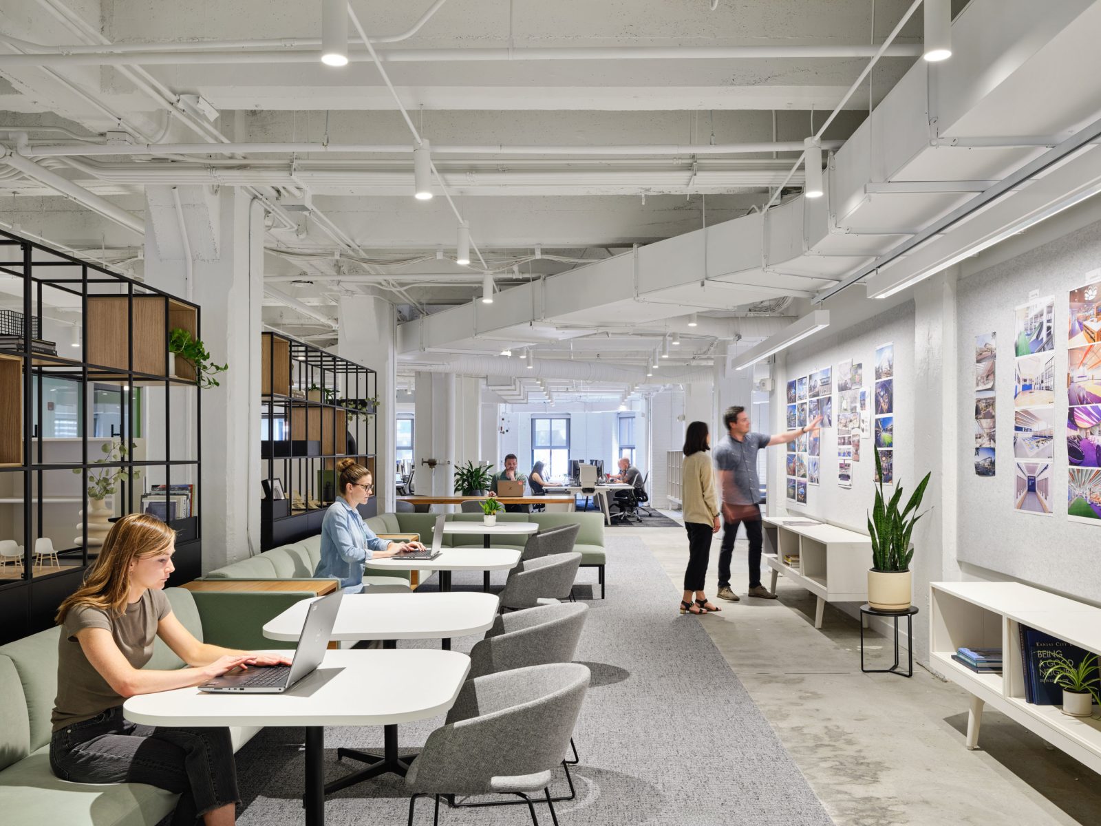 Open Collaborative area with cafe tables and benching, tall shelving dividers, art on walls, people working thruoughout the space with others or separately