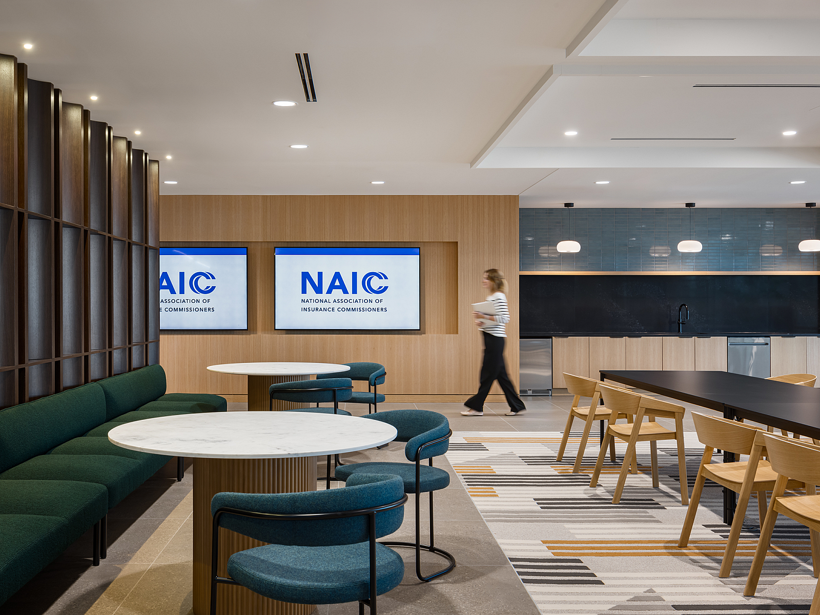 NAIC breakroom with modern banquette seating in rich green and blues, long darkwood tables with caramel colored wood chairs, NAIC logo on tv screens