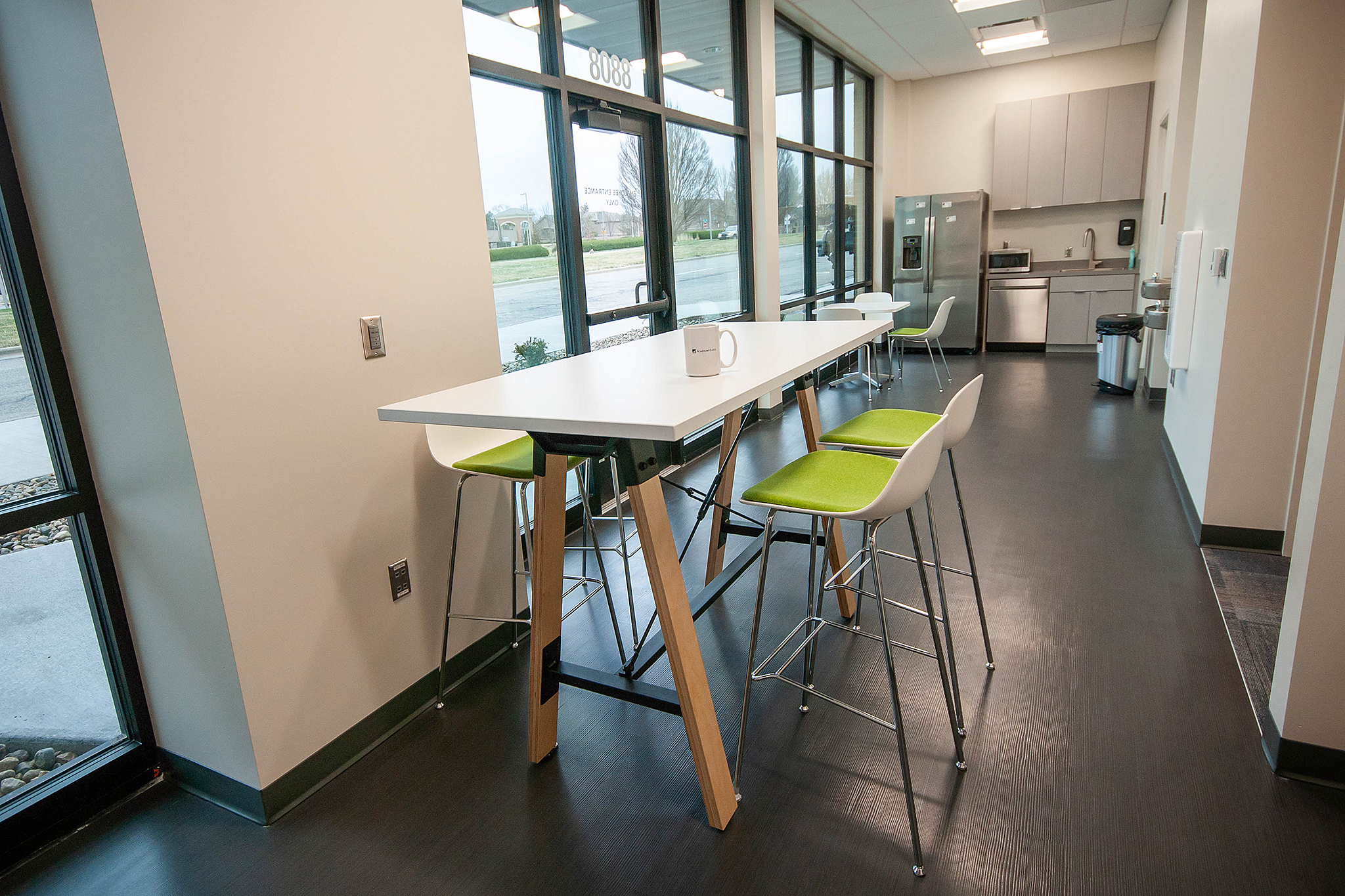 Academy Bank-small breakroom with high-top and low-top able with white/chrome-legged high stools and cafe chairs--both with green cushions.