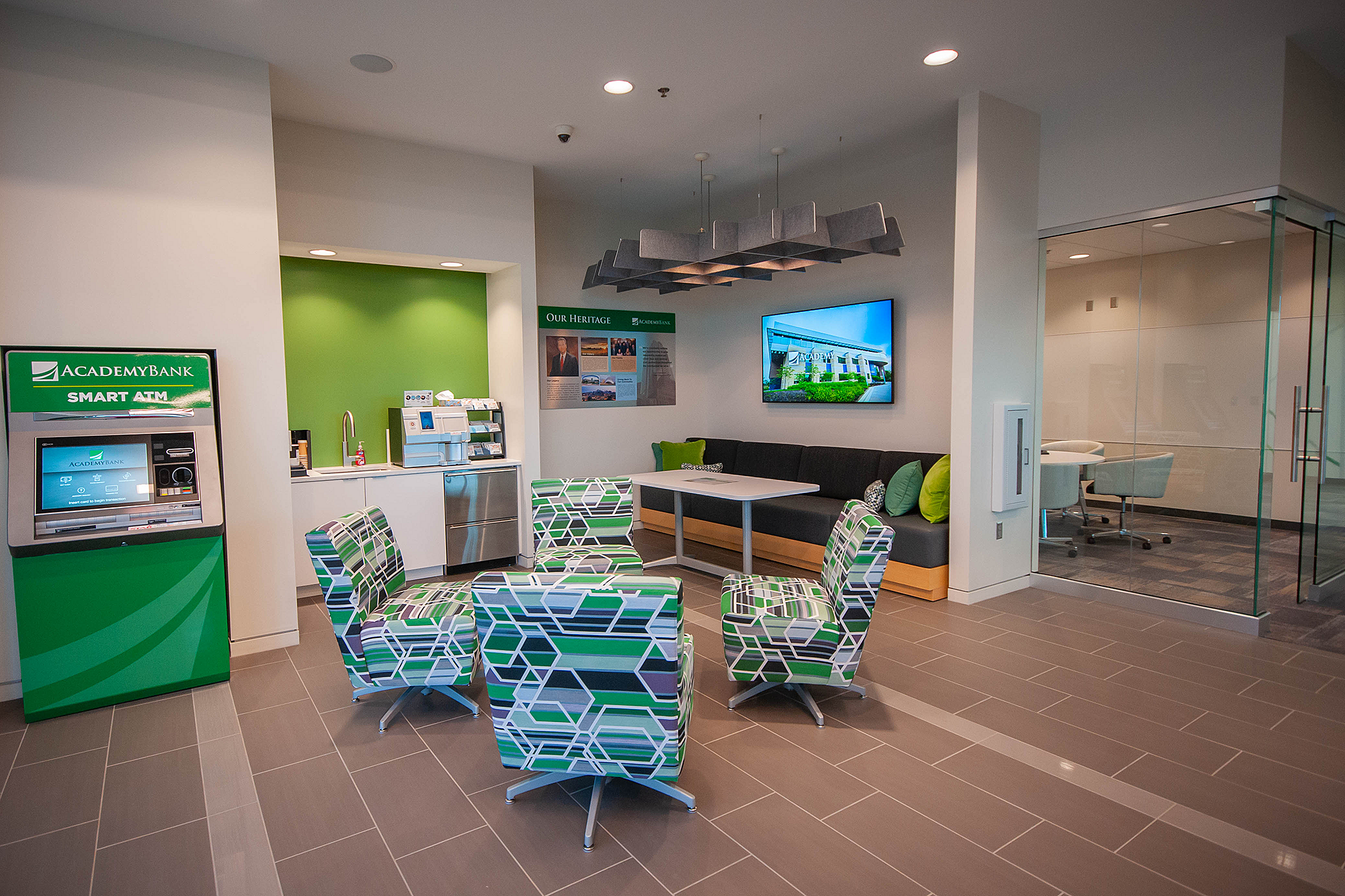 Adademy Bank lobby. Midback upholstered chairs with bold abstract green/black/white pattern, banquette seating and table under tv with green pillows