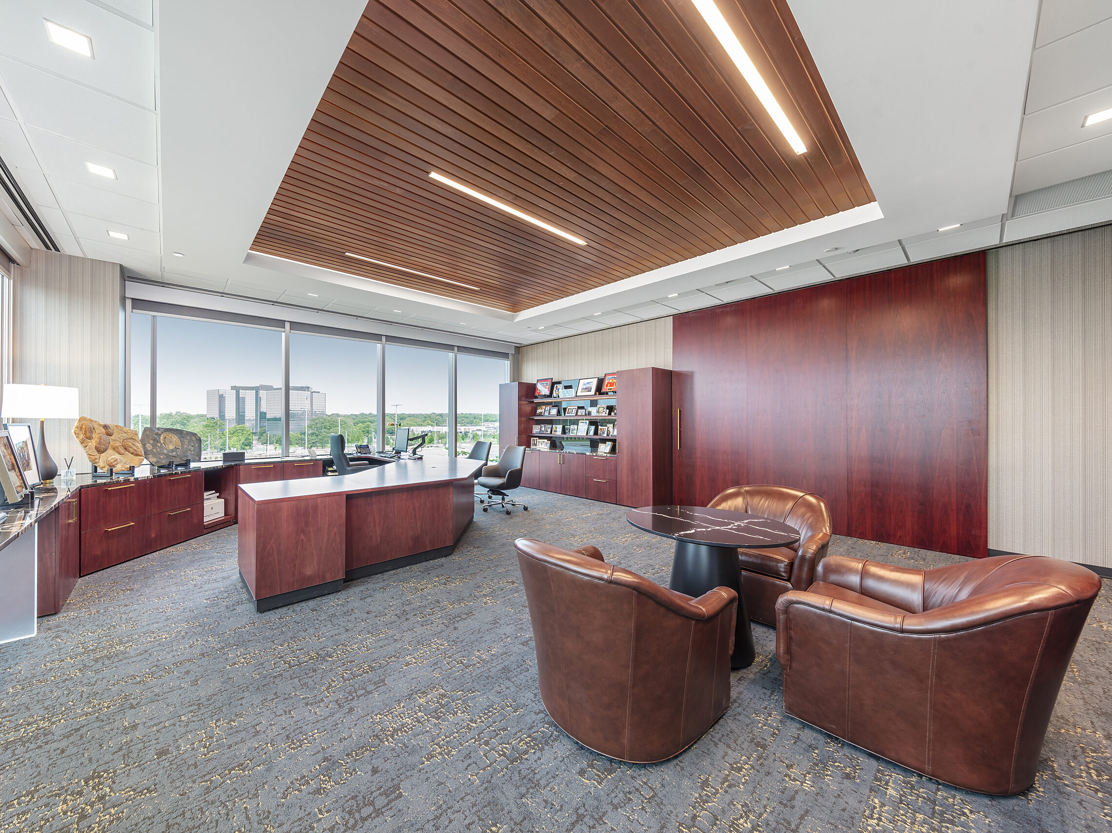 Corner executive office. Cherry woods. Large U-shaped desk, black leather task/guest chairs. Built-in bookshelf and 3-chair seating area with marble table