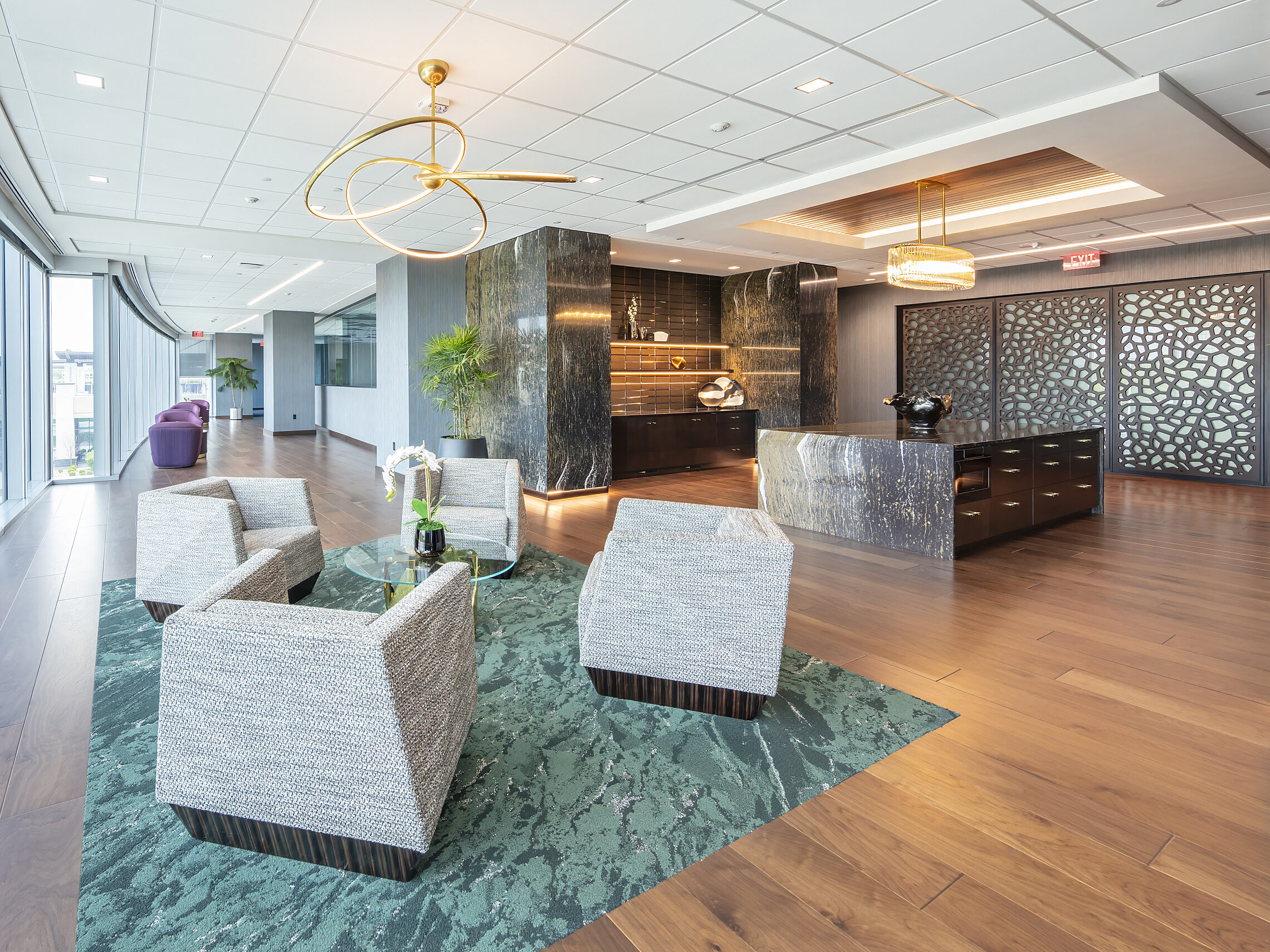 Lounge area with marbled walls & counter with metallic accents, green patterned area rugs on wood floor, black/white lounge chairs. Ornate sliding doors.