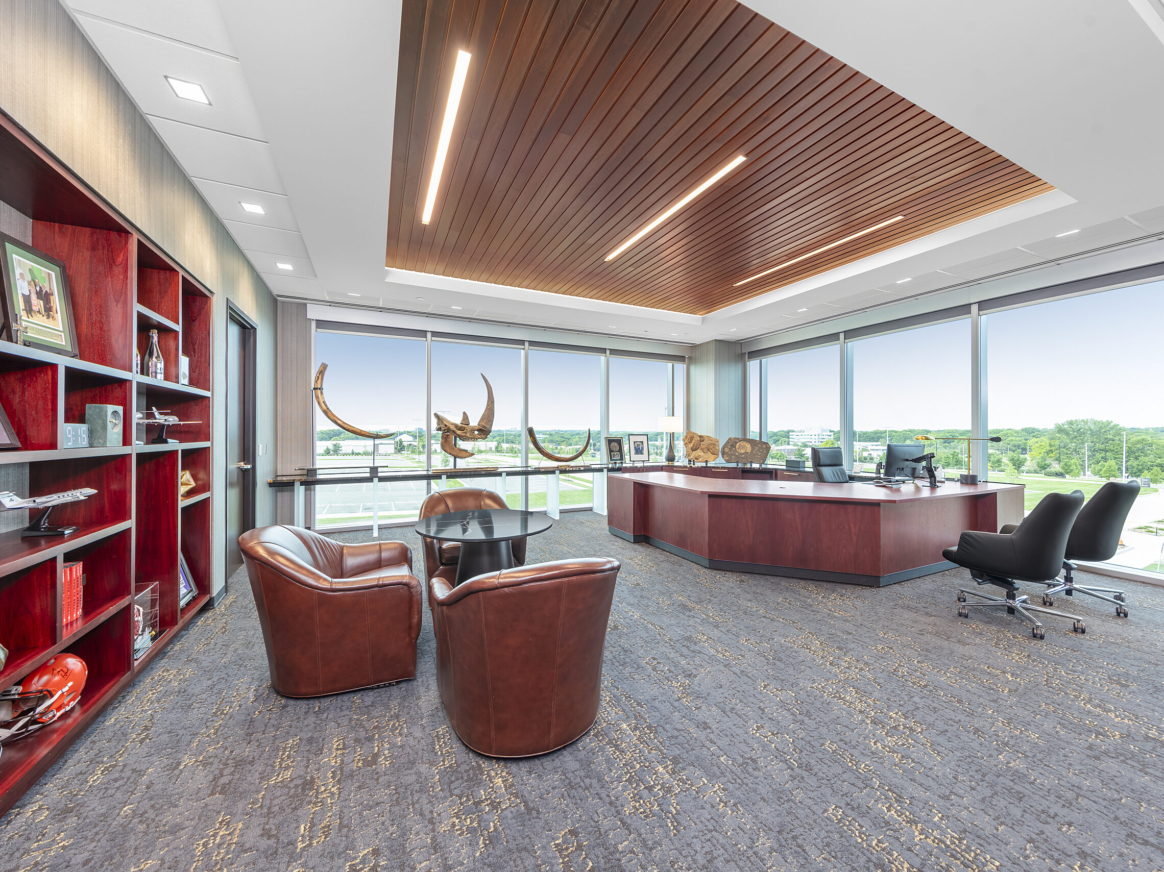 Corner executive office. Cherry woods. Large U-shaped desk, black leather task/guest chairs. Built-in bookshelf and 3-chair seating area with marble table
