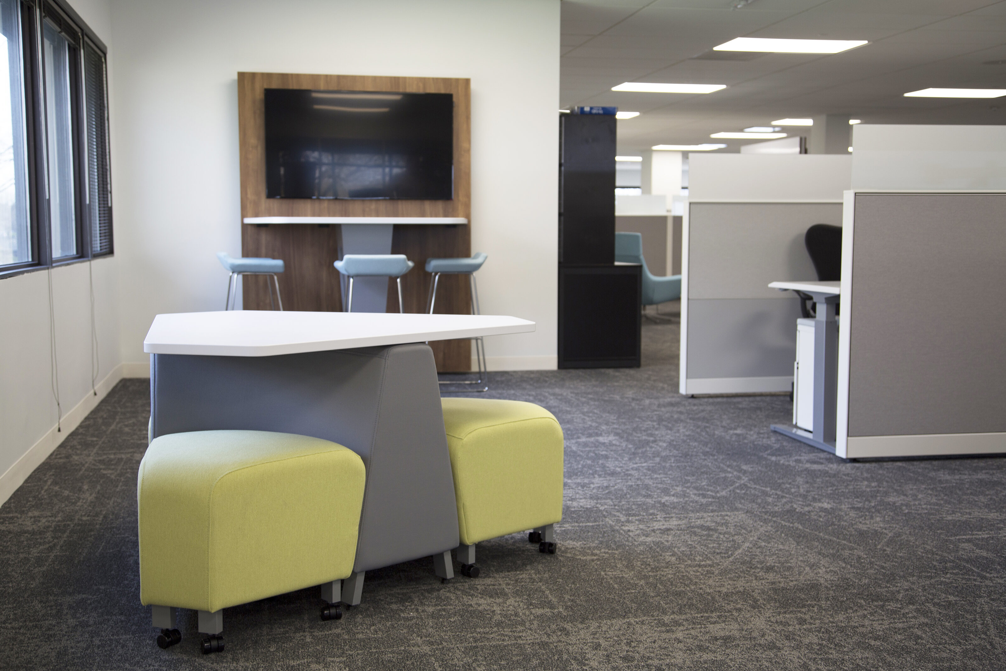 Lockton collaborative area.  A Huddle table with mounted tv and stools on one end and a low table with yellow beches around it