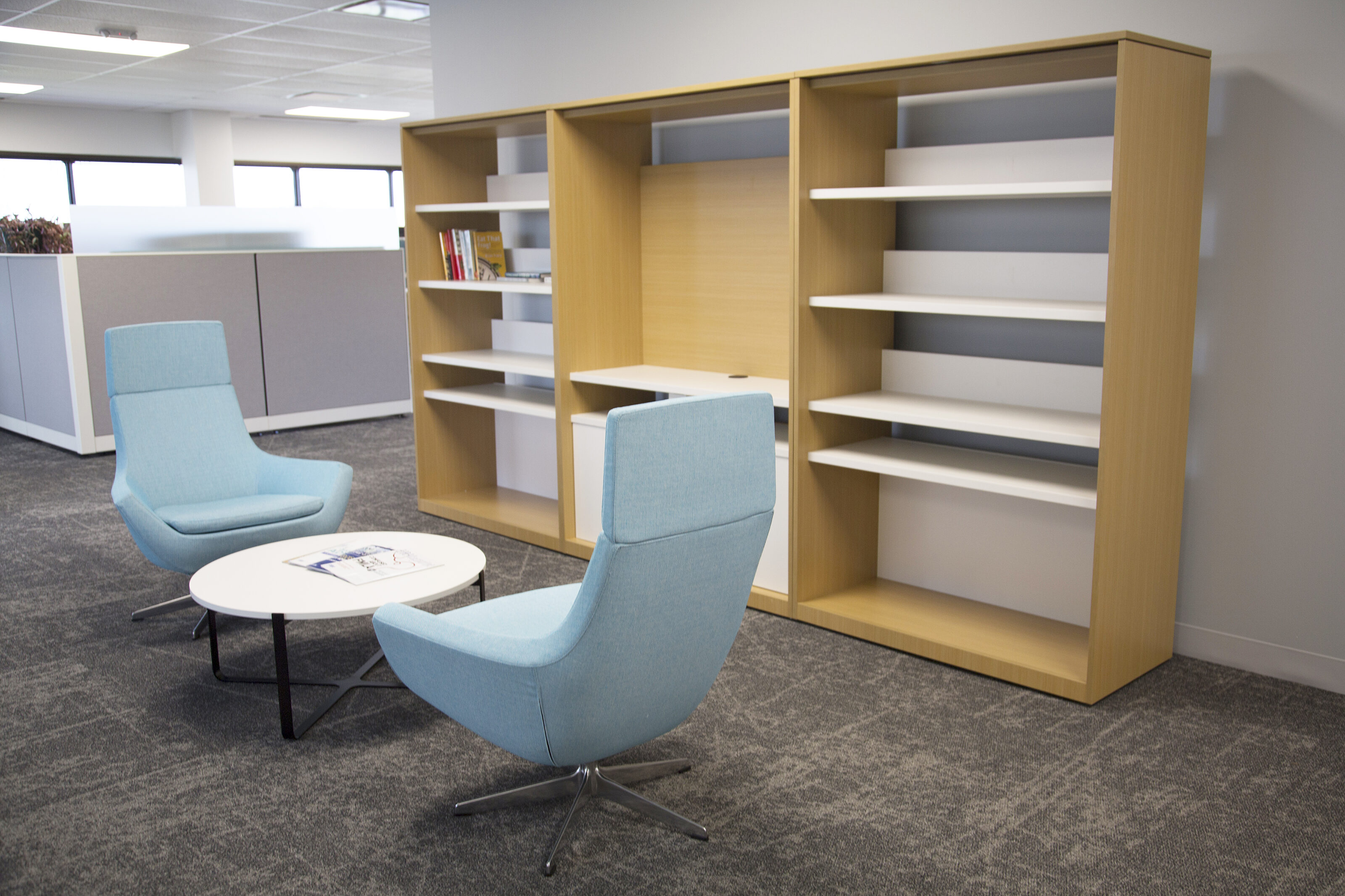Lockton-Collab area with three section bookcase, pale blue highback lounge chairs and small coffee table