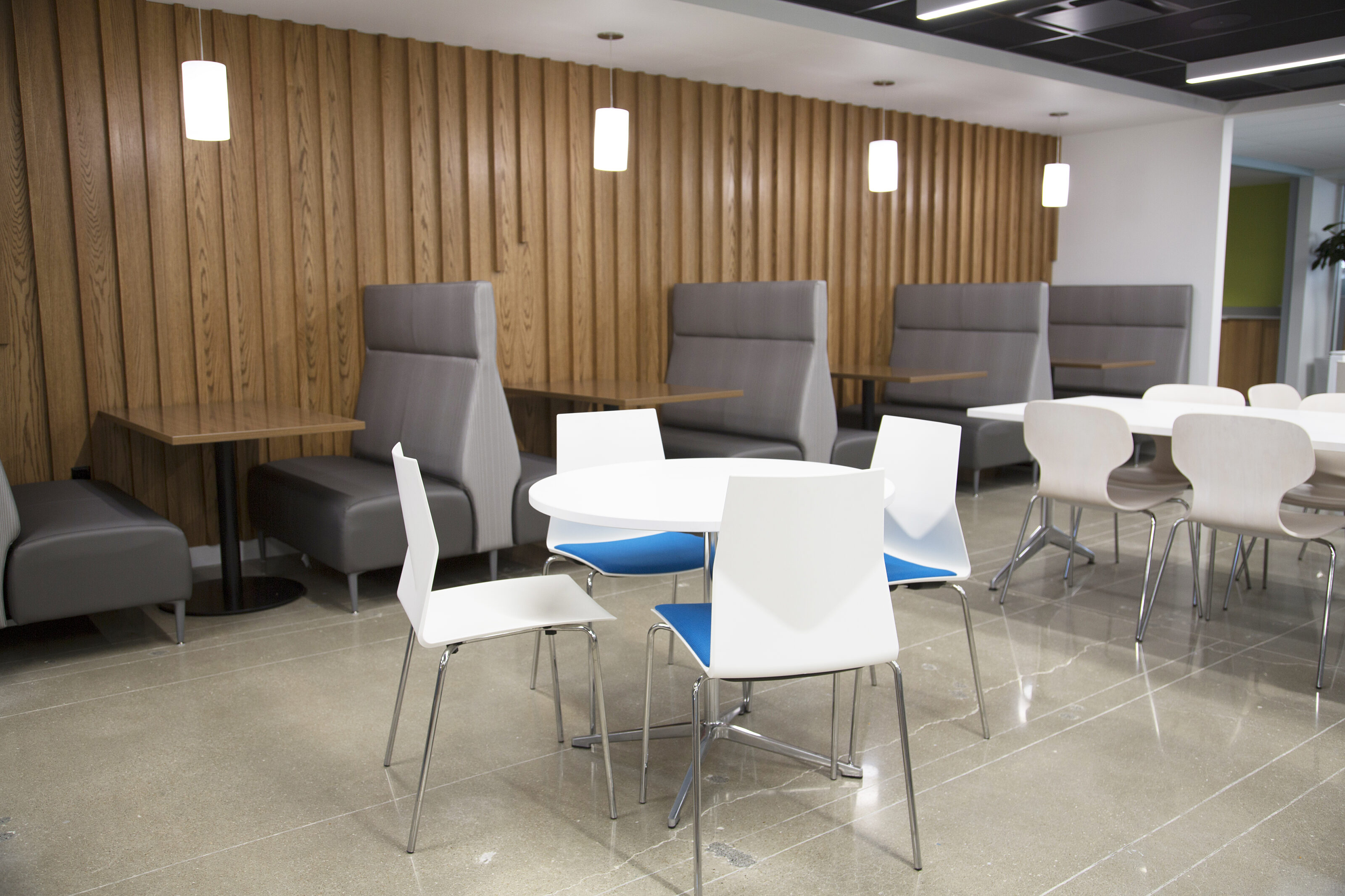 Lockton cafe-white cafe tables and chairs with blue seats. Tall grey booth seating along wooden planked wall with matching tables and white pendant lights