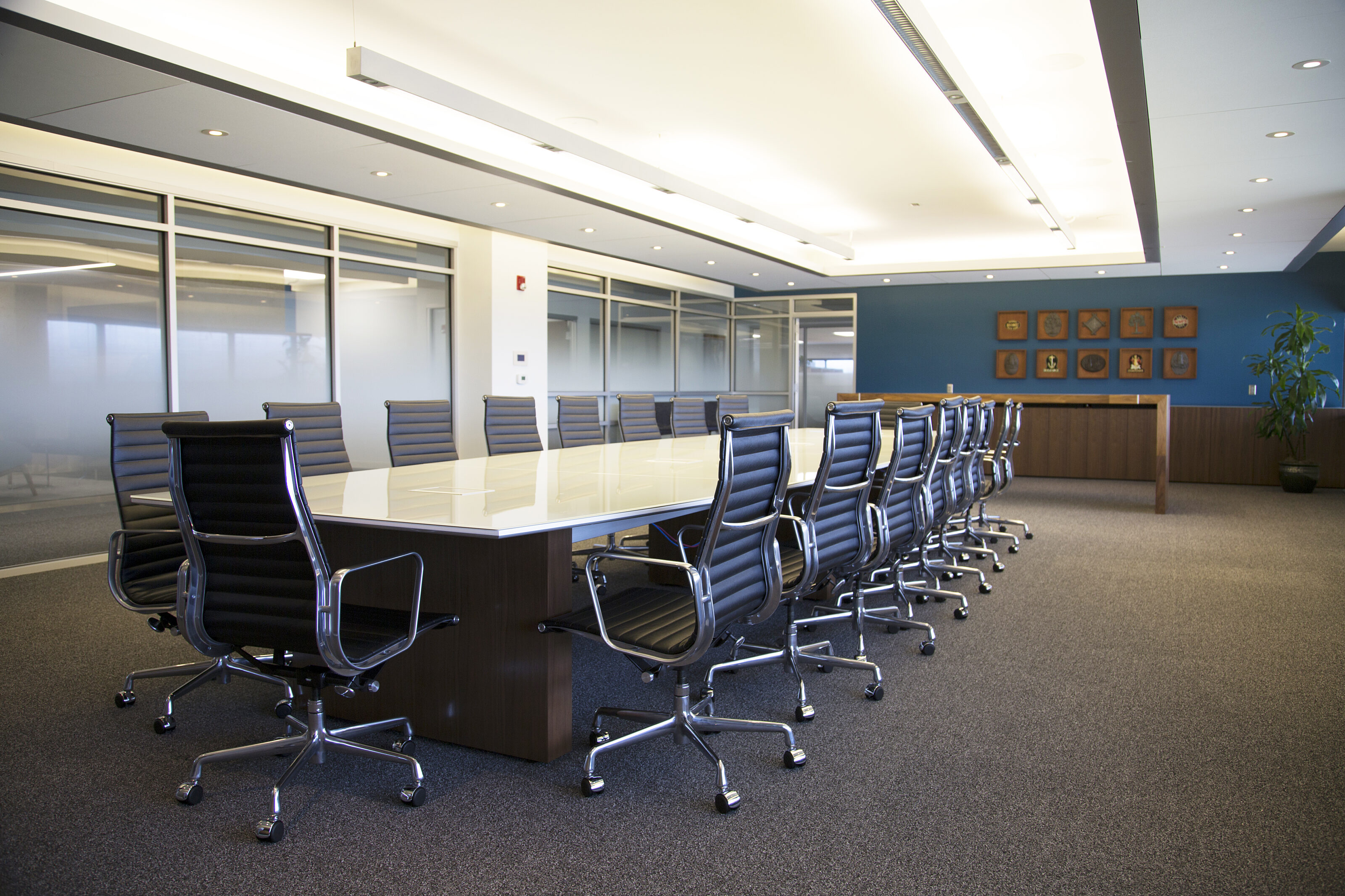 Lockton formal conference room with large table, dark blue Herman Miller Eames Aluminum chairs. Dark cabinetry and blue walls with artwork.