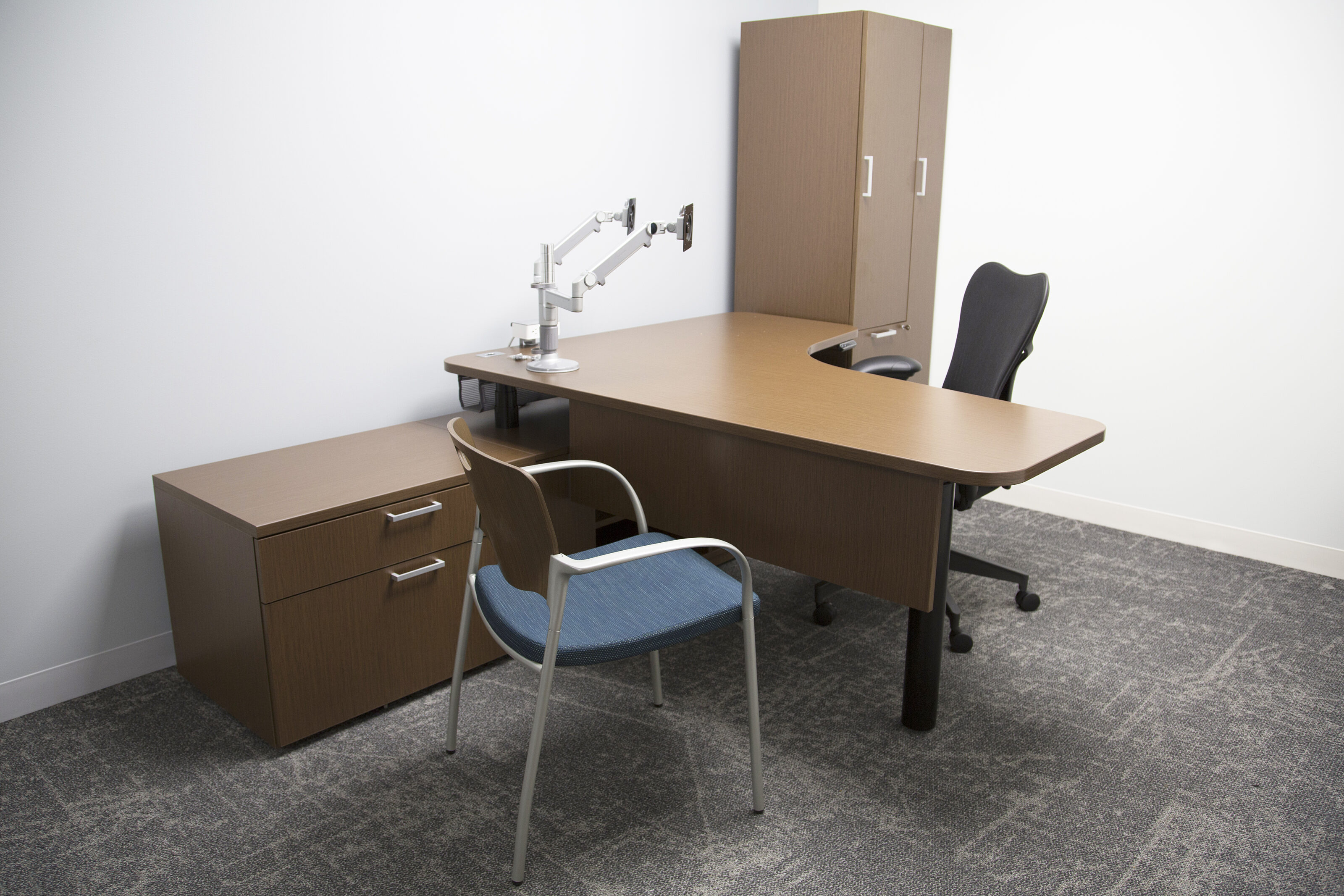 Lockton private office- Dark wood desk with monitor arms. Tall wooden storage locker and storage drawers. Aeron task chair and wood/blue guest chair.