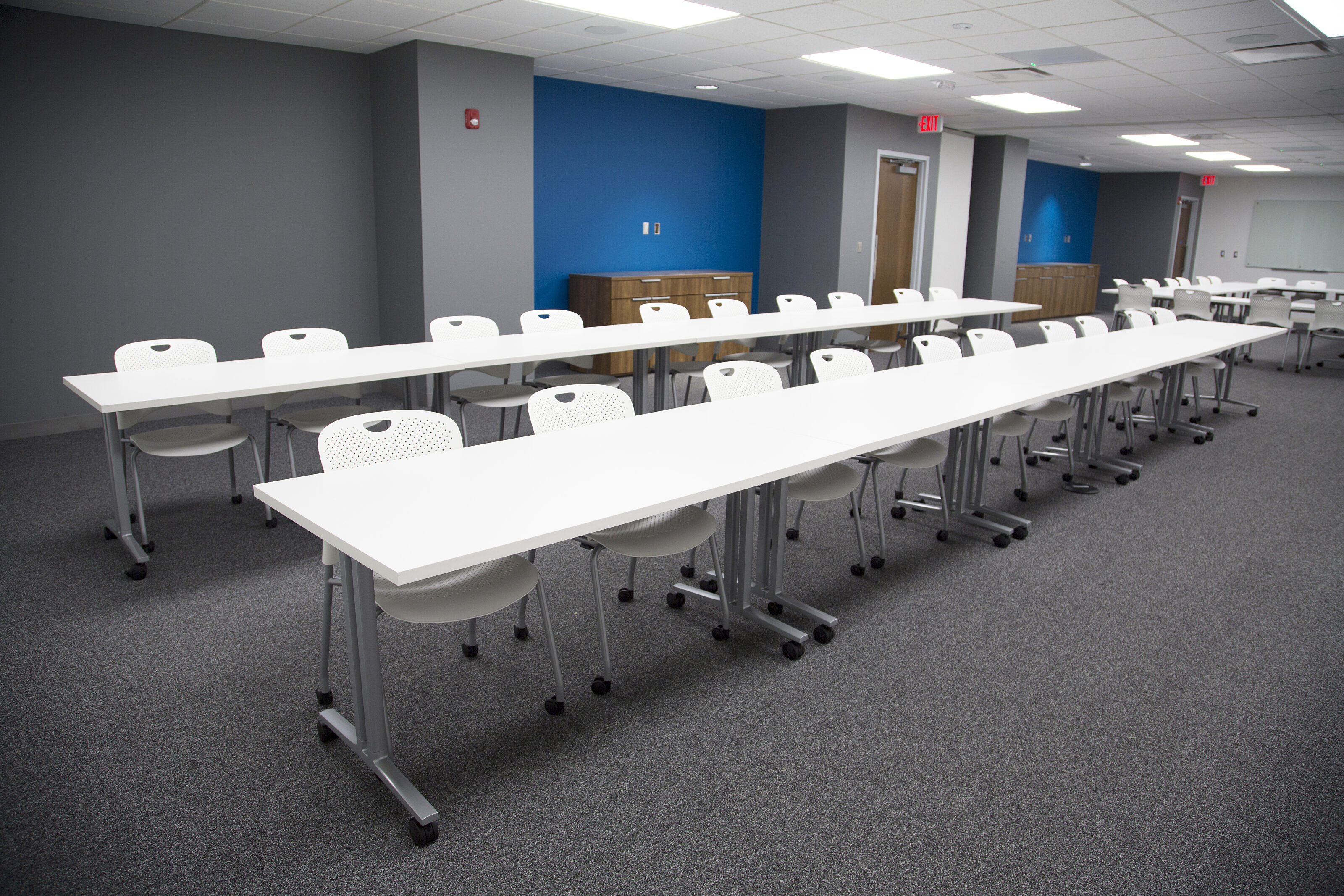 Lockton Affinity training room with multiple white tables with casters in two rows. White chairs with casters line and facie the front of the room.
