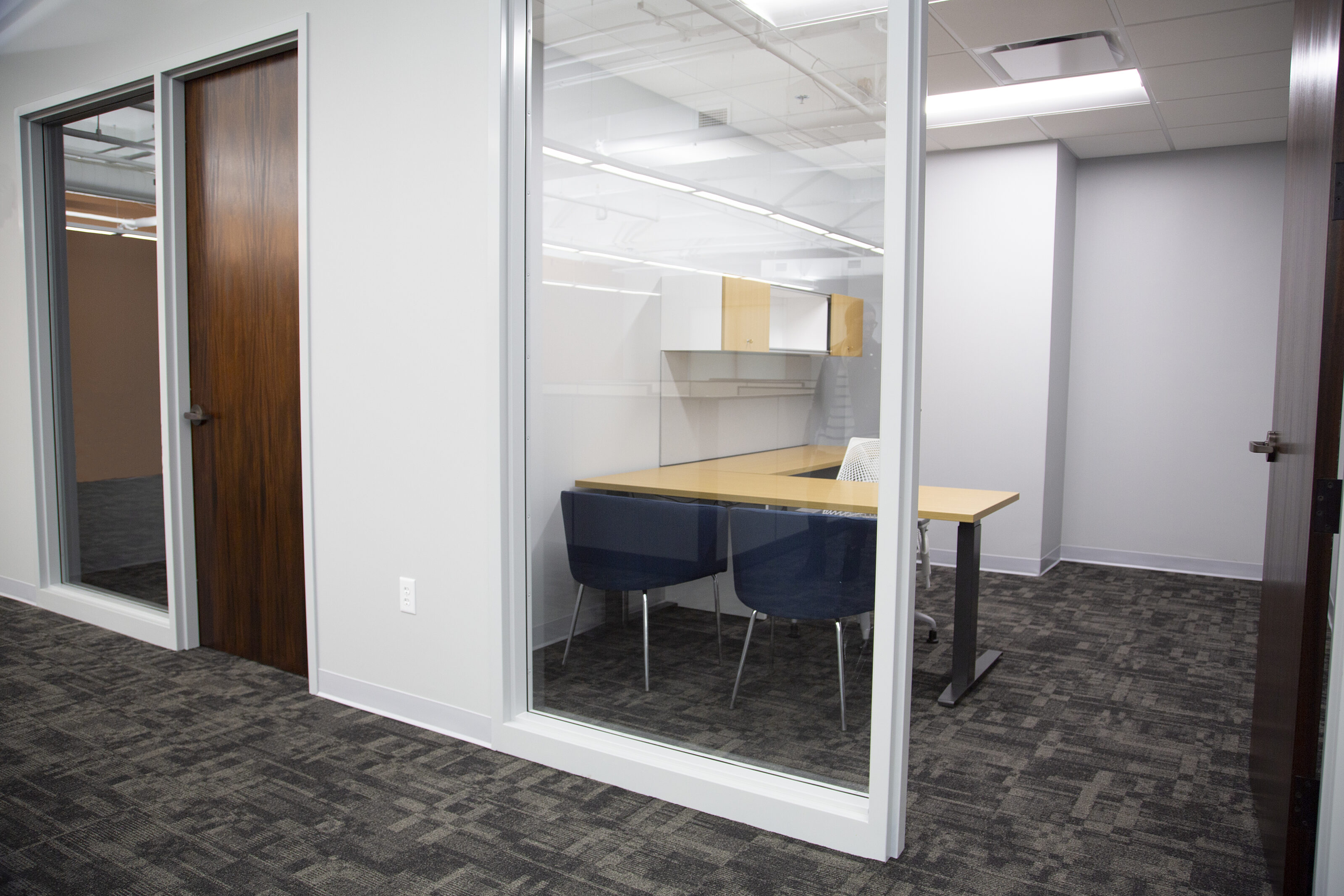 My Freight World - a private office with a height-adjustable L-shaped desk with light wood laminate and upper cabinets. Two blue u-shaped guest chairs.