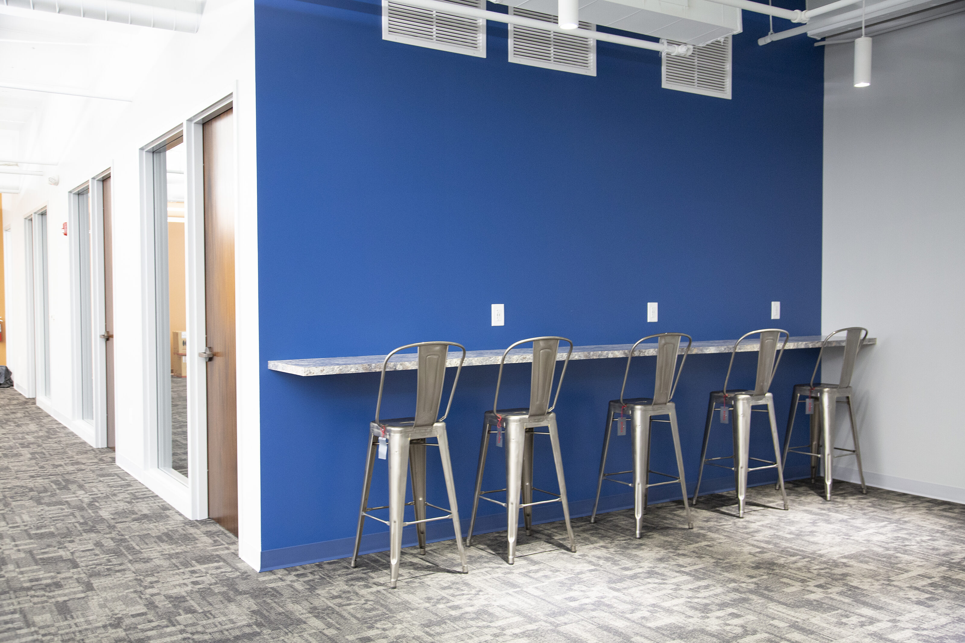 My Freight World - A simple marble counter and tall, aluminum stools with backs located on a blue wall outside a bank of private offices.
