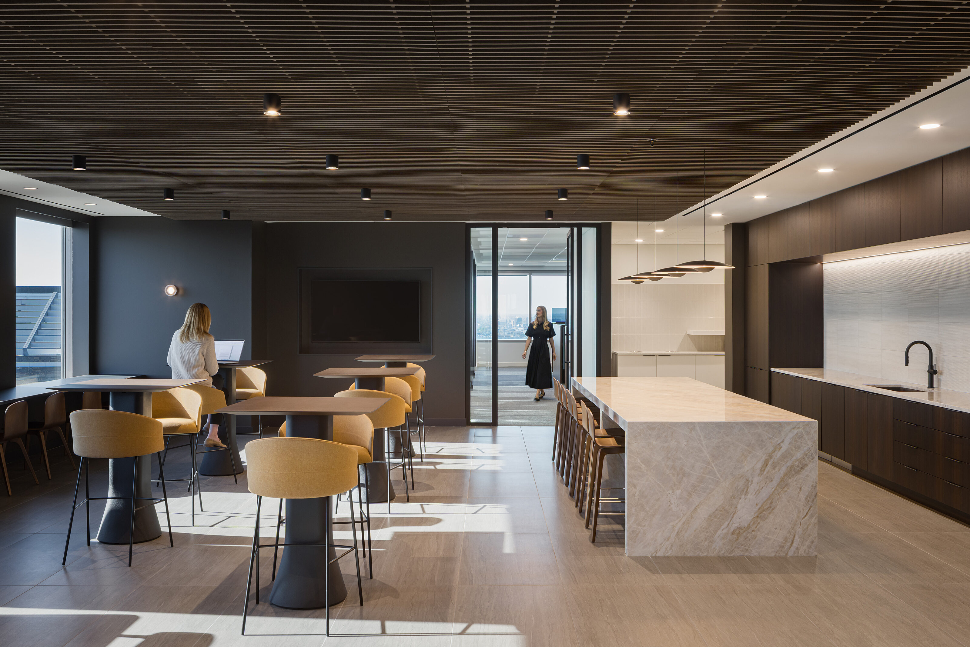Waypoint break room. Hightop cafe tables with tall stools and camel upholstery. A marble waterfall counter with wood counter stools in front of sink area.