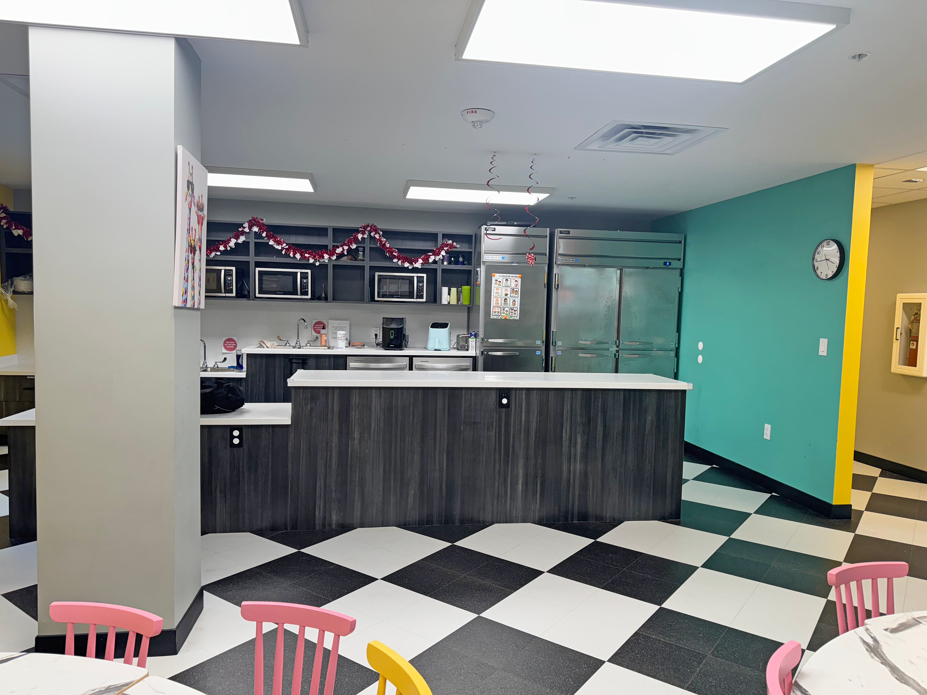 Riley ABA Dining room with black/white checked floor, a black counter with white top and teel walls. Kid sized tables with wood chairs in pink and yellow
