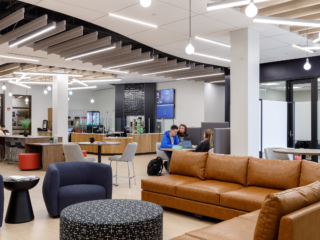 Student Lounge seating areas with students with small cafe in background. Brown leather sofa, blue lounge chairs, cafe tables with stools, rolling pouf's