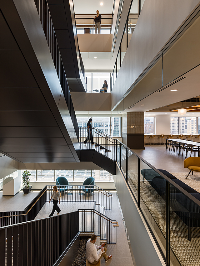 View of stairwell connecting 4 floors in office. Each floor has at least one employee on the either climbing, sitting on furniture or standing.