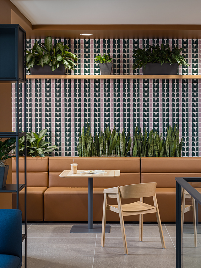 Brown leather mid-back banquette seating nook with accent wallpaper inside. Plants line shelf and top of seating, square cafe table with light wood chair