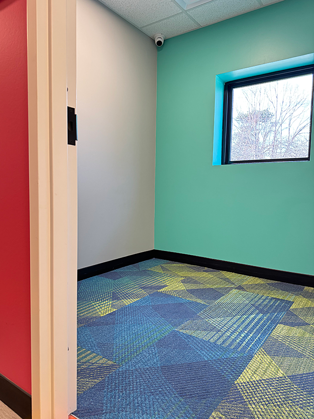 Riley ABA: Small office with a colorful patterned carpet in blue and yellow, with a teal accent wall with a single window