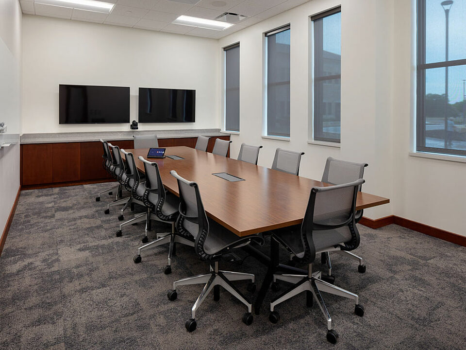 Conference room with table and twelve chairs. Two mounted tvs on far end.