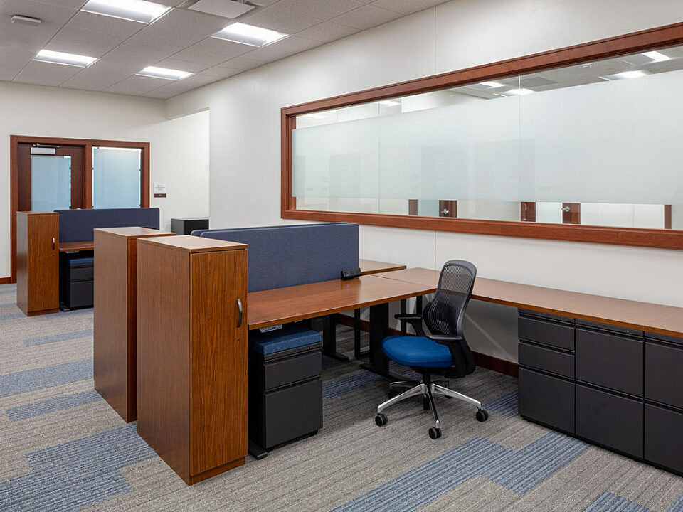 A line of height-adjustable wood finish workstations with tower storage unit, as well as mobile pedestal storage in front of a frosted window.
