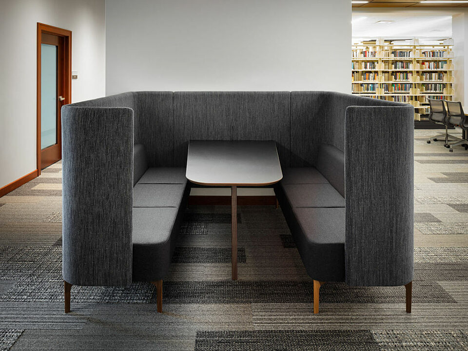 Law library - Dark grey 6-person booth with table and high back.  Library shelves with books and other tables can be seen off to side behind it.