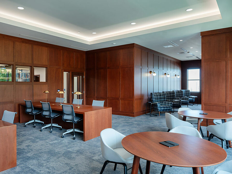 Wood paneled study room with 3 seating areas: cafe tables and chairs, waterfall tables with rolling chairs and blue/white plaid lounge chairs in back